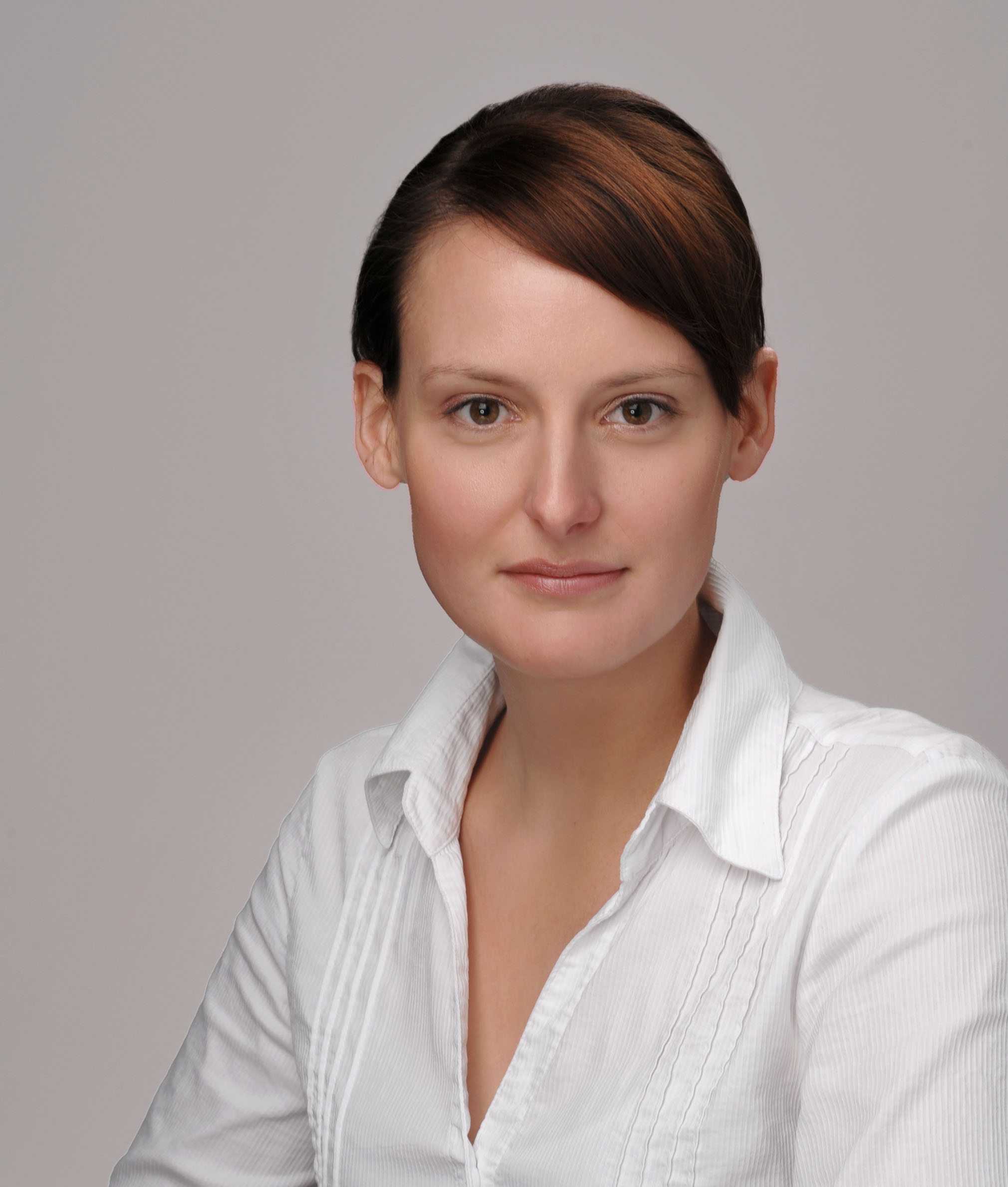 Das Foto zeigt ein Businessbild einer jungen Frau in einem weißem Oberteil vor hellgrauem Hintergrund mit gesunden Hauttönen